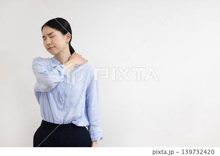 白い壁の前で肩に手を当てて痛そうな表情をする日本人女性 白い壁の前で肩に手を当てて痛そうな表情をする日本人女性 139732420