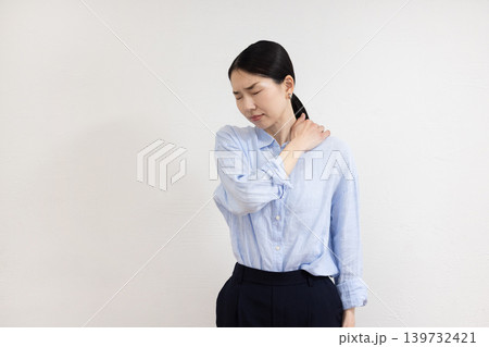 白い壁の前で肩に手を当てて痛そうな表情をする日本人女性 白い壁の前で肩に手を当てて痛そうな表情をする日本人女性 139732421