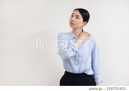 白い壁の前で肩に手を当てて痛そうな表情をする日本人女性 白い壁の前で肩に手を当てて痛そうな表情をする日本人女性 139732422
