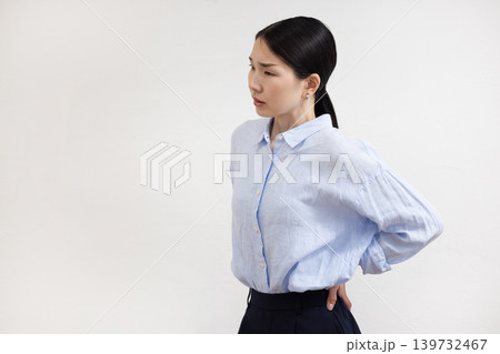 白い壁の前で腰に手を当てて痛そうな表情をする日本人女性 白い壁の前で腰に手を当てて痛そうな表情をする日本人女性 139732467