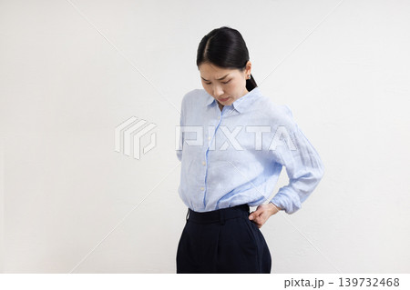 白い壁の前で腰に手を当てて痛そうな表情をする日本人女性 白い壁の前で腰に手を当てて痛そうな表情をする日本人女性 139732468