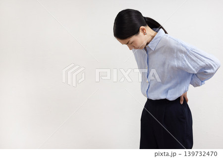 白い壁の前で腰に手を当てて痛そうな表情をする日本人女性 白い壁の前で腰に手を当てて痛そうな表情をする日本人女性 139732470