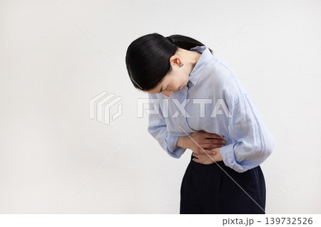 白い壁の前でお腹に手を当てて痛そうな表情をする日本人女性 白い壁の前でお腹に手を当てて痛そうな表情をする日本人女性 139732526