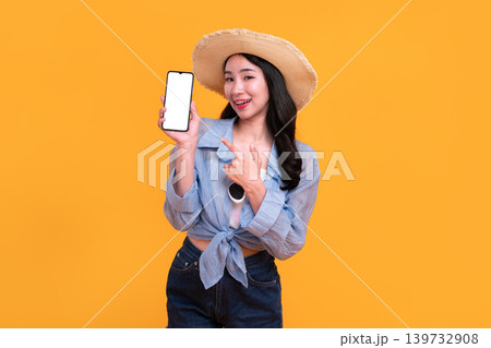 Happy Asian woman woman tourist holding a blank phone isolated on yellow background. Happy Asian woman woman tourist holding a blank phone isolated on yellow background. 139732908