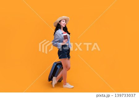 Happy Asian woman traveler standing and holding suitcase isolated on yellow background, Tourist girl having cheerful holiday trip concept, Full body composition. Happy Asian woman traveler standing and holding suitcase isolated on yellow background, Tourist girl having cheerful holiday trip concept, Full body composition. 139733037
