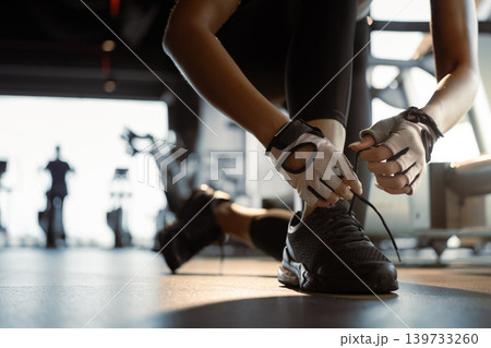 Close-up of sportswoman tying shoelace in a gym. Close-up of sportswoman tying shoelace in a gym. 139733260