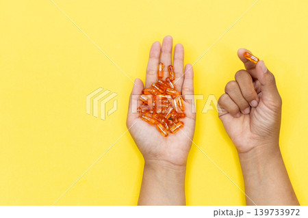 Close up of a person's hand holding several golden softgel capsules. Concept of taking daily dose of vitamin or fish oil supplement for healthcare and wellness. Close up of a person's hand holding several golden softgel capsules. Concept of taking daily dose of vitamin or fish oil supplement for healthcare and wellness. 139733972