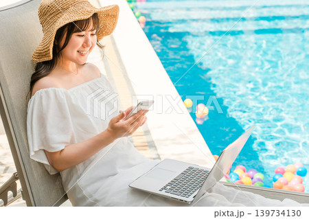 プールサイドのリクライニングチェアに座りスマホを操作する若いアジア人女性 プールサイドのリクライニングチェアに座りスマホを操作する若いアジア人女性 139734130