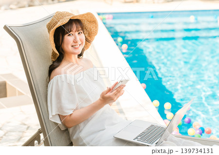 プールサイドのリクライニングチェアに座りスマホを操作する若いアジア人女性 プールサイドのリクライニングチェアに座りスマホを操作する若いアジア人女性 139734131