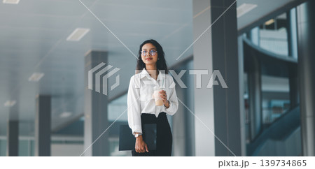 Professional woman in eyeglasses holding iced coffee and a clipboard in a modern office corridor, expressing confident corporate lifestyle, work break, career focus, and everyday productivity. Professional woman in eyeglasses holding iced coffee and a clipboard in a modern office corridor, expressing confident corporate lifestyle, work break, career focus, and everyday productivity. 139734865