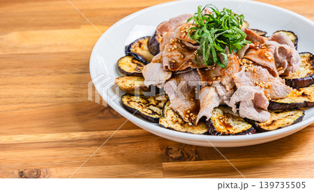木目テーブルの上に置かれた焼きなすの豚しゃぶのせ 139735505