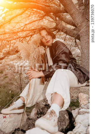Woman nature pampas sitting on stones under a tree in warm sunset light Woman nature pampas sitting on stones under a tree in warm sunset light 139736070