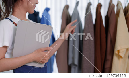 Asian women entrepreneur checking clothing inventory for live streaming online shop selling fashion garments retail merchant business holding digital tablet at 139736336