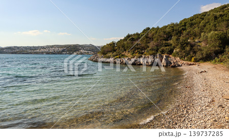 Bitez bay coastline with clear aegean sea water, rocky shore, lush green hill, and cityscape on horizon Bitez bay coastline with clear aegean sea water, rocky shore, lush green hill, and cityscape on horizon 139737285