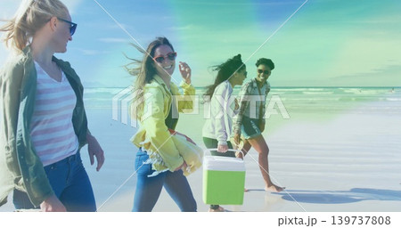 Walking group of four women carrying green-and-white cooler on wet sand at beach, wearing jackets Walking group of four women carrying green-and-white cooler on wet sand at beach, wearing jackets 139737808
