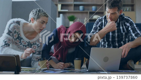 Collaborating adults wearing headscarf kneeling and studying laptop on floor with papers and coffee Collaborating adults wearing headscarf kneeling and studying laptop on floor with papers and coffee 139737860