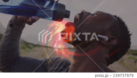 Tilting man drinking from blue bottle on dune, wearing dark-gray top, white earbud, red-orange glow Tilting man drinking from blue bottle on dune, wearing dark-gray top, white earbud, red-orange glow 139737879