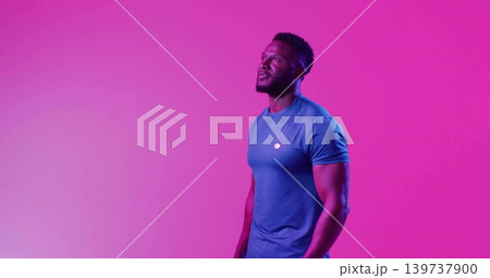 Standing muscular man wearing fitted blue athletic tee against magenta gel backdrop, copy space 139737900