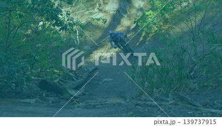 Riding cyclist taking right turn on wooded hillside trail with mountain bike, helmet, roots Riding cyclist taking right turn on wooded hillside trail with mountain bike, helmet, roots 139737915