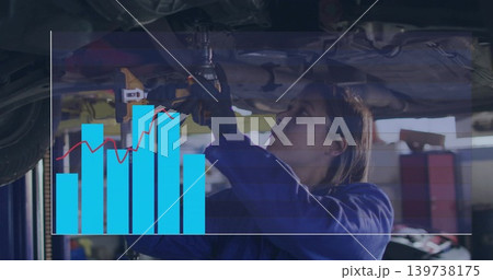 Tightening mechanic in blue coverall under raised vehicle at garage, using drill with chart overlay Tightening mechanic in blue coverall under raised vehicle at garage, using drill with chart overlay 139738175