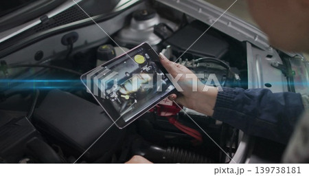 Holding tablet, technician in work jacket showing engine map over open car hood with red cable 139738181