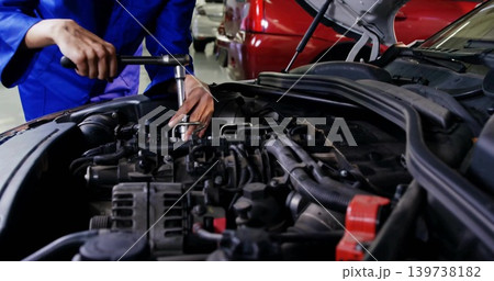 Tightening woman mechanic in blue coveralls using socket wrench on engine bay in shop, red terminal Tightening woman mechanic in blue coveralls using socket wrench on engine bay in shop, red terminal 139738182