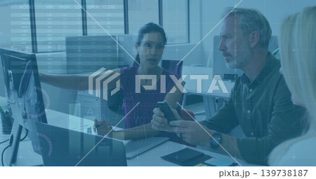 Pointing woman in sleeveless purple top leading meeting with team in office with phone and monitors Pointing woman in sleeveless purple top leading meeting with team in office with phone and monitors 139738187