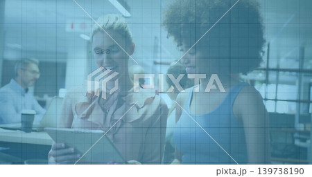 Holding tablet, two colleagues reviewing content in modern office in ruffled blouse and blue top Holding tablet, two colleagues reviewing content in modern office in ruffled blouse and blue top 139738190