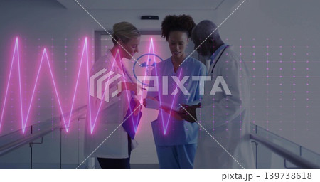 Discussing three medics in lab coats and scrubs, reviewing tablet in hospital hallway, magenta ECG 139738618