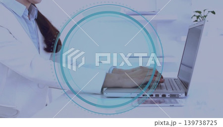 Typing clinician wearing white lab coat using silver laptop at clinical desk, HUD and plant Typing clinician wearing white lab coat using silver laptop at clinical desk, HUD and plant 139738725