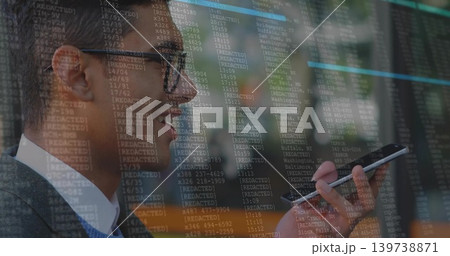 Speaking man in business attire holding smartphone near mouth at modern office, with code overlay Speaking man in business attire holding smartphone near mouth at modern office, with code overlay 139738871