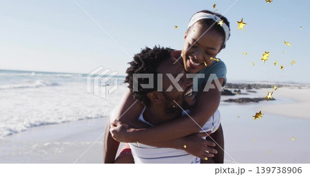 Smiling man in striped shirt piggybacking woman with headband on beach, with gold star overlays Smiling man in striped shirt piggybacking woman with headband on beach, with gold star overlays 139738906