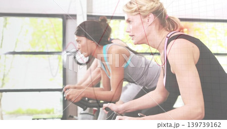 Pedaling blonde woman in black tank pink-strap on bike in studio, with red earphone, copy space Pedaling blonde woman in black tank pink-strap on bike in studio, with red earphone, copy space 139739162