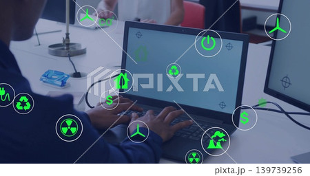 Typing worker wearing dark shirt at workstation, using laptop with green icons and blue tissue pack Typing worker wearing dark shirt at workstation, using laptop with green icons and blue tissue pack 139739256