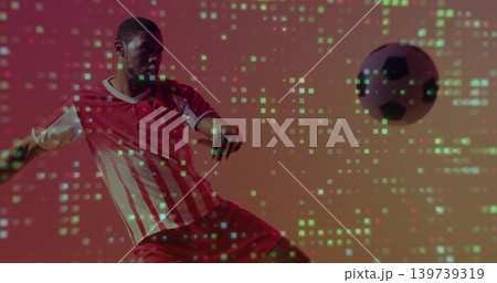 Kicking adult player in red-striped jersey red shorts striking ball in studio with green pixelation Kicking adult player in red-striped jersey red shorts striking ball in studio with green pixelation 139739319