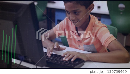 Typing boy in orange-striped polo leaning in school computer lab, using black keyboard and monitor 139739469