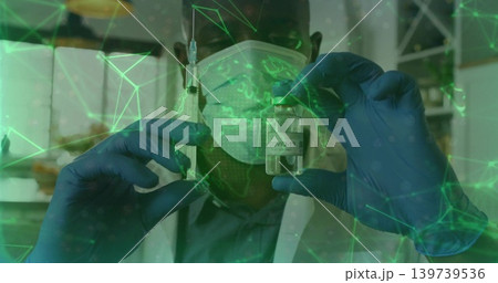 Presenting worker in lab coat, surgical mask and gloves holding syringe and COVID-19 vial at clinic Presenting worker in lab coat, surgical mask and gloves holding syringe and COVID-19 vial at clinic 139739536
