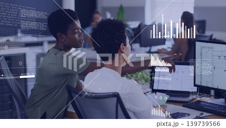 Pointing coworker in green top guiding colleague in white blouse at office, dual monitors overlays Pointing coworker in green top guiding colleague in white blouse at office, dual monitors overlays 139739566