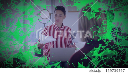 Presenting woman in red-striped shirt leading meeting at table with laptop, papers, green overlay Presenting woman in red-striped shirt leading meeting at table with laptop, papers, green overlay 139739567