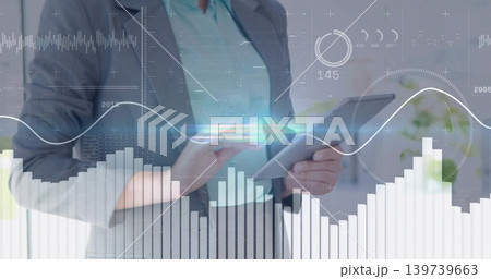 Holding woman executive in grey blazer teal blouse tapping tablet at desk, with data overlays 139739663
