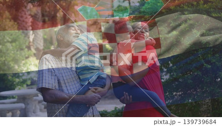 Smiling checked-shirt grandpa holding boy, red-dress woman holding girl in park, flag overlay Smiling checked-shirt grandpa holding boy, red-dress woman holding girl in park, flag overlay 139739684