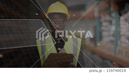 Standing warehouse tech wearing yellow hardhat hi-vis vest holding clipboard, checking with grid UI 139740019