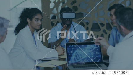 Collaborating medical team in scrubs and white coats in training room, using VR headset and laptop 139740073