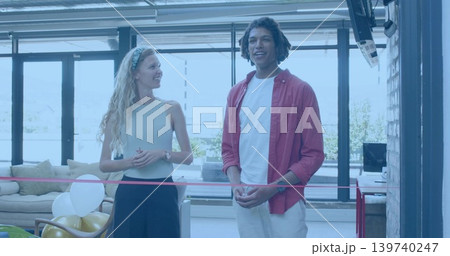 Standing two hosts in casual clothes smiling in modern lounge near windows, red ribbon and balloons Standing two hosts in casual clothes smiling in modern lounge near windows, red ribbon and balloons 139740247