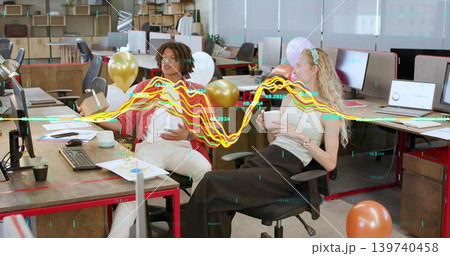 Celebrating coworkers wearing casual wear sharing cake at office with balloons and waveform Celebrating coworkers wearing casual wear sharing cake at office with balloons and waveform 139740458