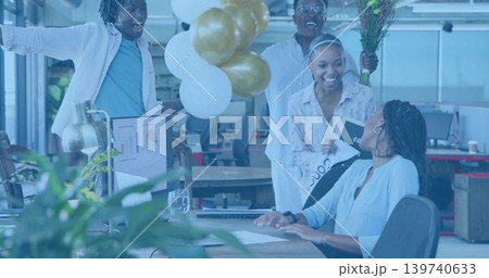 Presenting team celebrating seated coworker in casual business attire at office with balloons Presenting team celebrating seated coworker in casual business attire at office with balloons 139740633