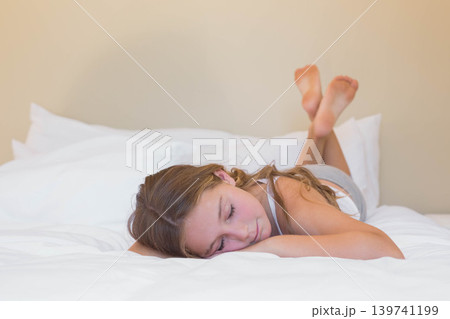 Female child lying face down on white sheets, wearing sleeveless top, shorts against beige wall Female child lying face down on white sheets, wearing sleeveless top, shorts against beige wall 139741199