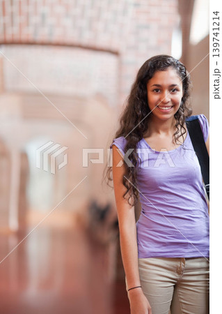Female teen standing on right in brick hall, in purple T-shirt, holding backpack strap, copy space Female teen standing on right in brick hall, in purple T-shirt, holding backpack strap, copy space 139741214