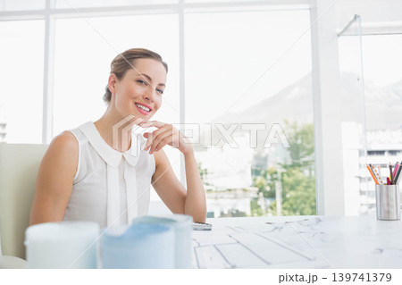 Woman wearing white blouse smiling and posing at desk with building plans, smartphone, copy space Woman wearing white blouse smiling and posing at desk with building plans, smartphone, copy space 139741379