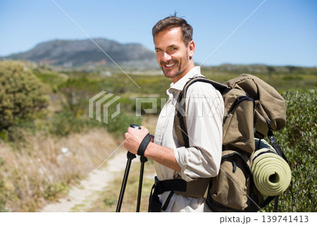 Mature man standing on trail holding trekking poles with backpack and rolled pad, copy space Mature man standing on trail holding trekking poles with backpack and rolled pad, copy space 139741413